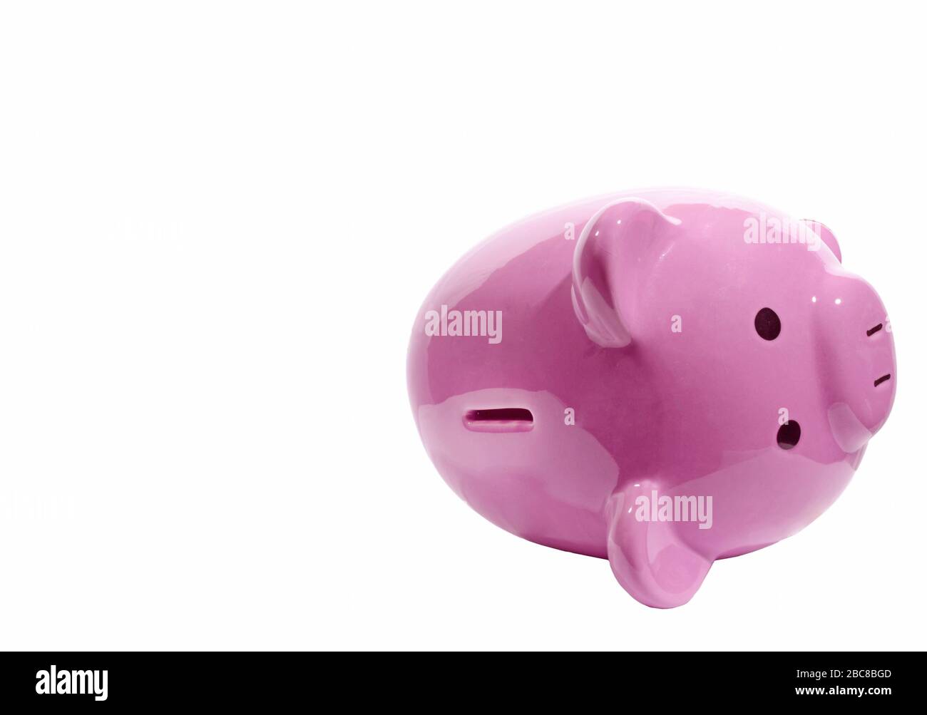 Horizontal shot of a pink piggy bank lying on its side with the slot facing toward the camera on the right side of the picture.  Lots of copy space on Stock Photo