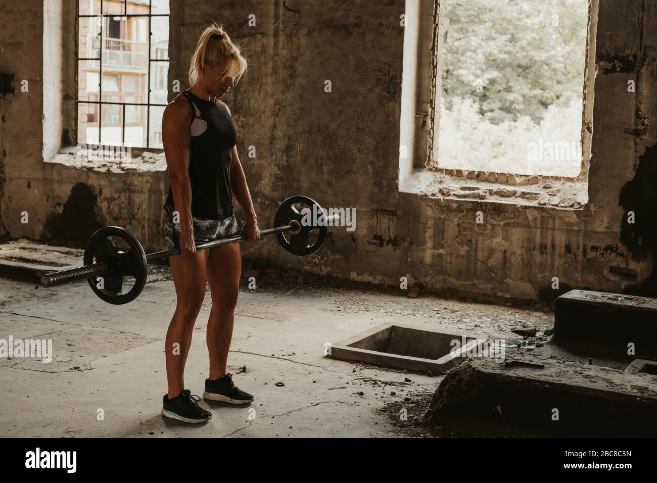 Athletic blonde woman holding weights in deadlift in an old building. Beautiful day Stock Photo