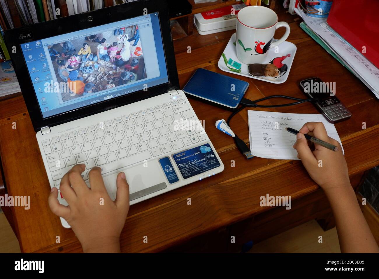 A close up shot of a person's hand, a laptop, an external harddisk, a cup of coffee, a cellphone, a note and a pen. Ready to work at home. Stock Photo