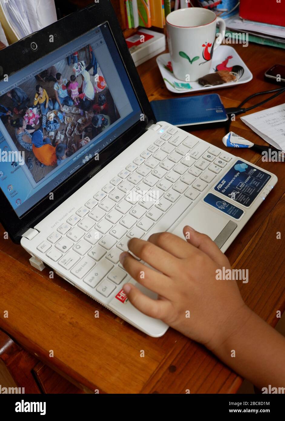 A close up shot of a person's hand that edit a photo with a laptop, an external harddisk and a cup of coffee. Ready to work remotely at home. Stock Photo