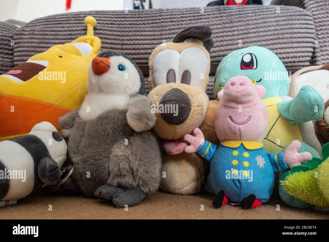 Cuddly toys resembling various cartoon characters lined up along a settee. Stock Photo