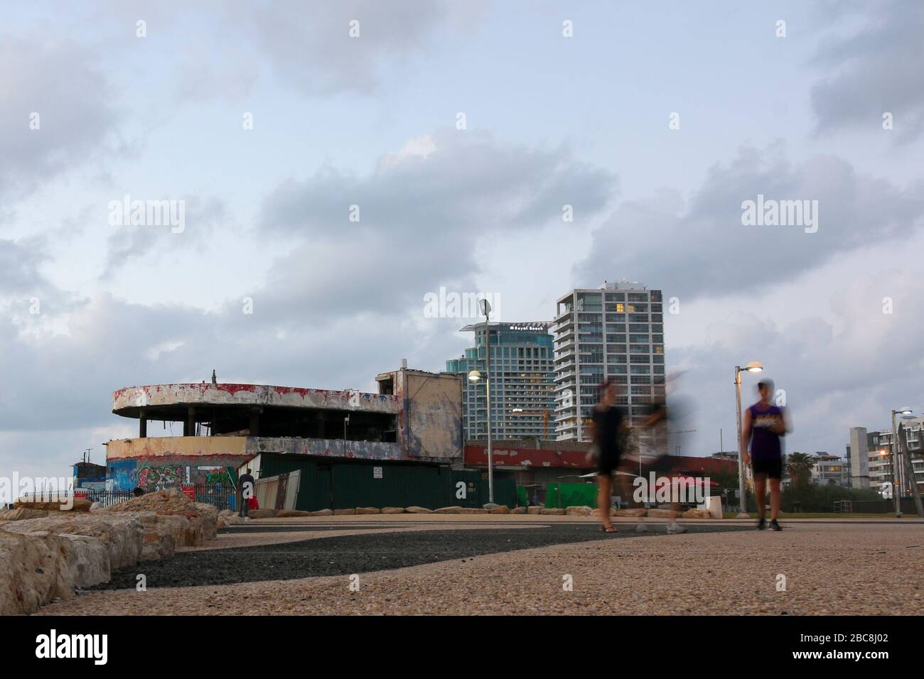 Israel, Tel Aviv, tourists walk along the Tel Aviv seafront, in the background is the ruins of the Dolphy nightclub Stock Photo