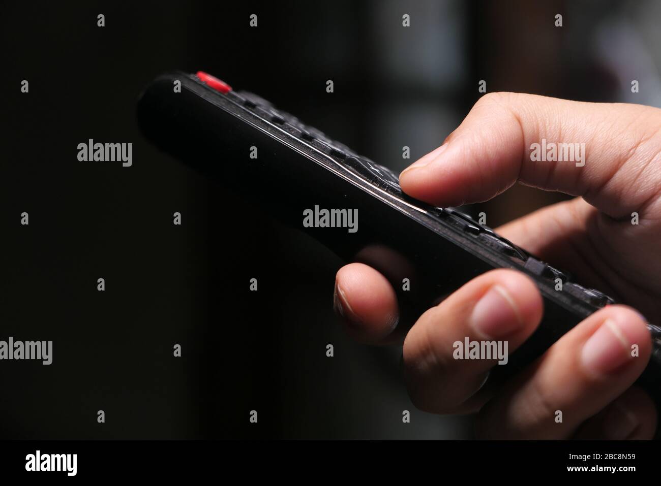 Hand holding remote control sitting on sofa . Stock Photo