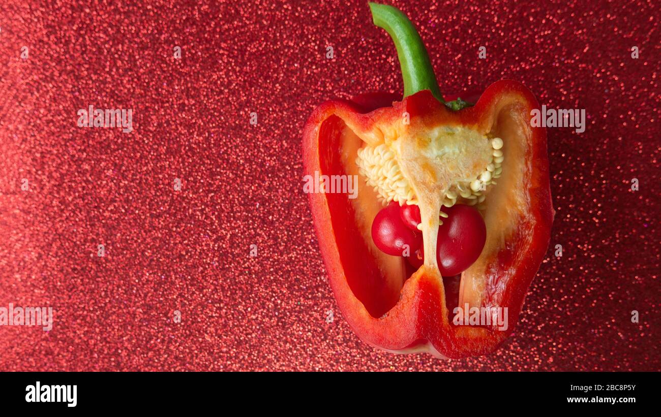 Two small bell peppers growing inside a red one, red glitter backdrop. Stock Photo