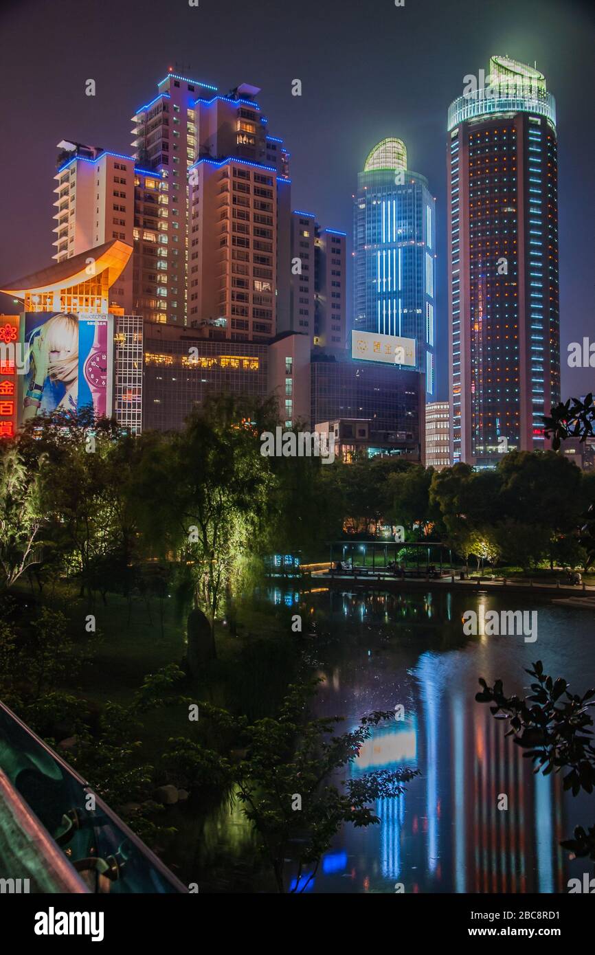 Shanghai, Xuhui, China - May 3, 2010: Night portrait. Colorfully lighted skyscrapers peep over dark trees of Xujiahui Park. Stock Photo