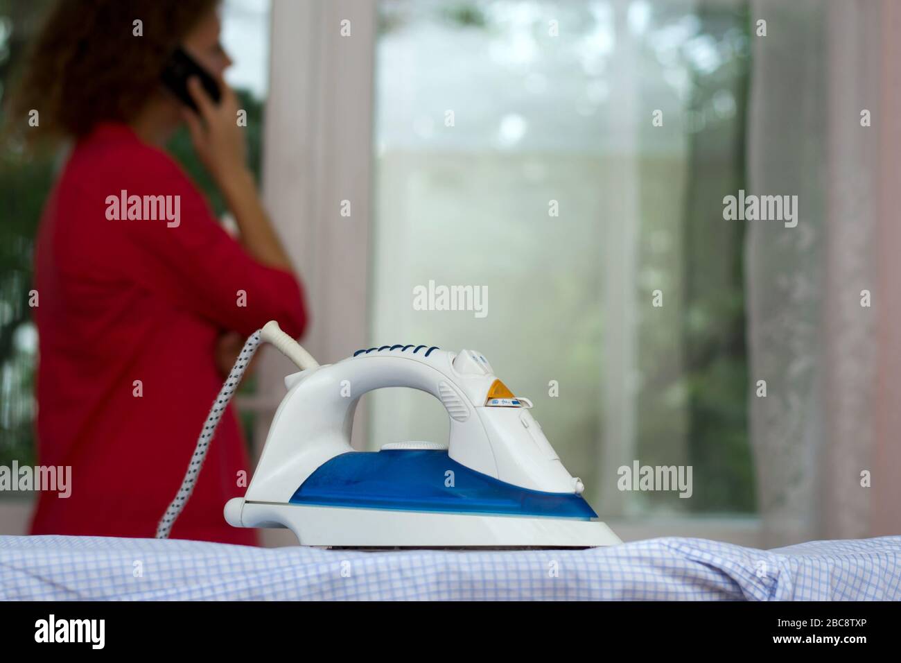 Girl talking on the phone forgetting about the iron on the ironing board Stock Photo