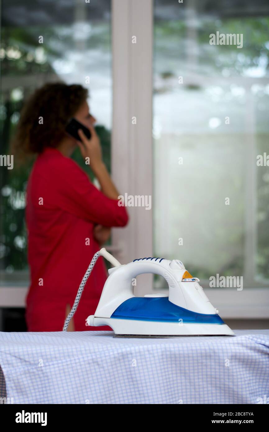Girl talking on the phone forgetting about the iron on the ironing board Stock Photo