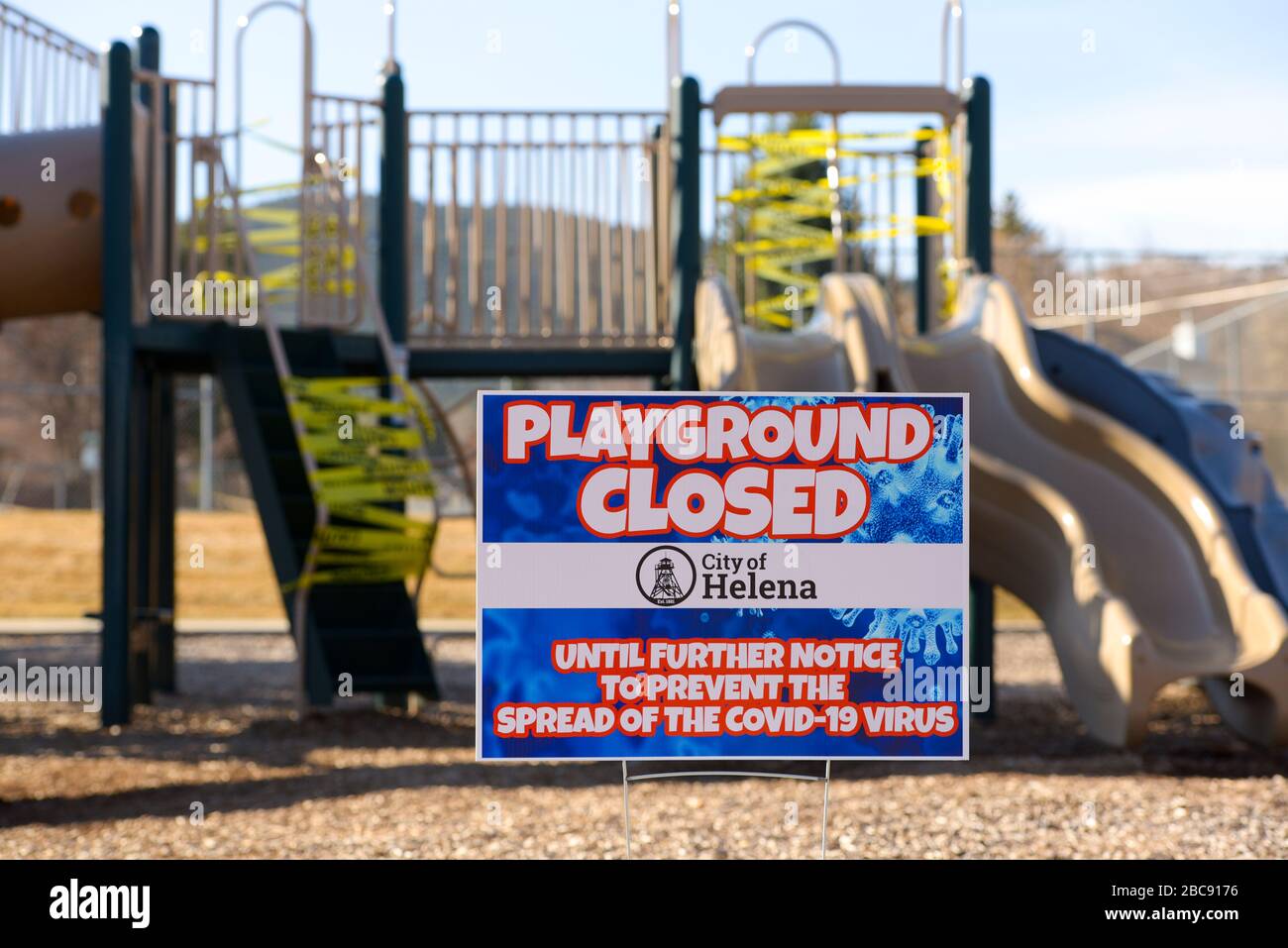 Helena, Montana - March 30, 2020: Playground closed sign with yellow caution tape wrapped around slide & stairs to prevent spread of Coronavirus. Stock Photo