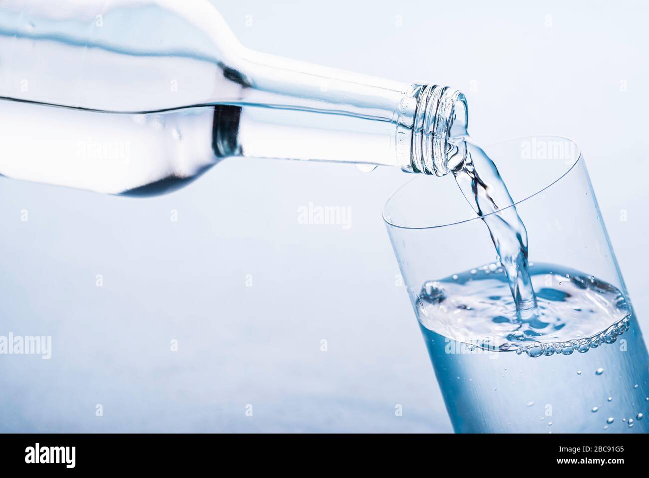 Pouring water from a glass bottle to a glass on a blue background