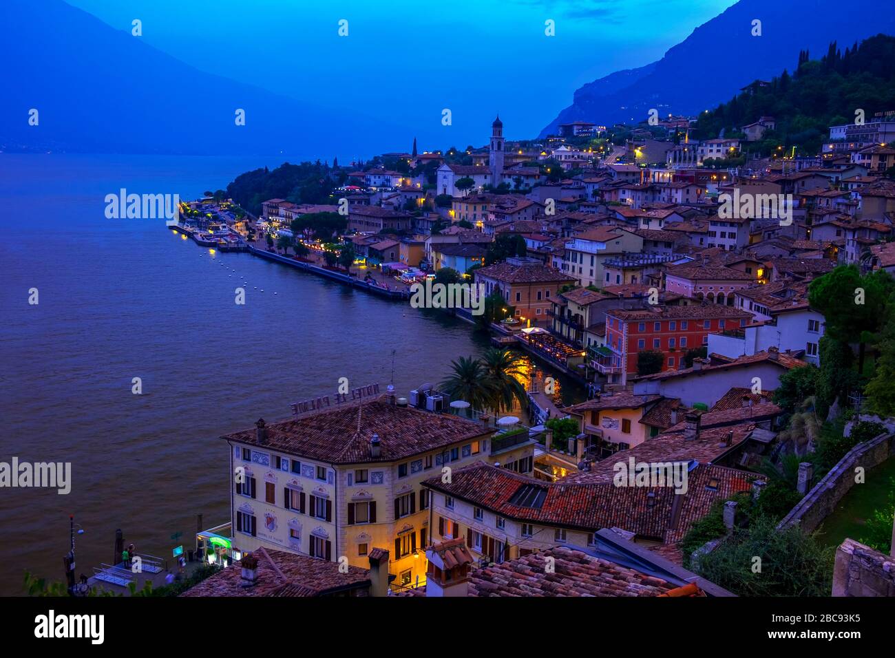 Lake Garda boardwalk with houses, tourists and boats in Torbole, Italy Stock Photo
