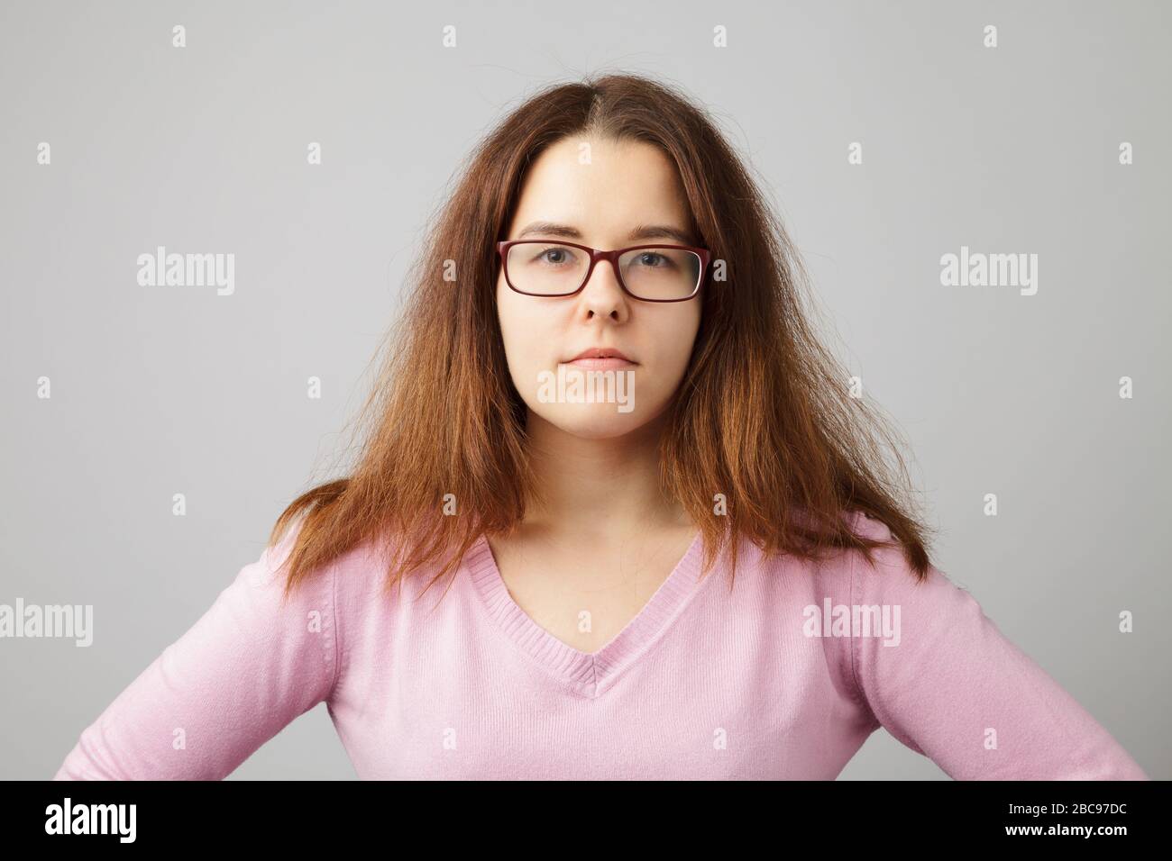 Young shaggy woman in eye glasses wearing pink cardigan. Head and shoulders portrait. Stock Photo