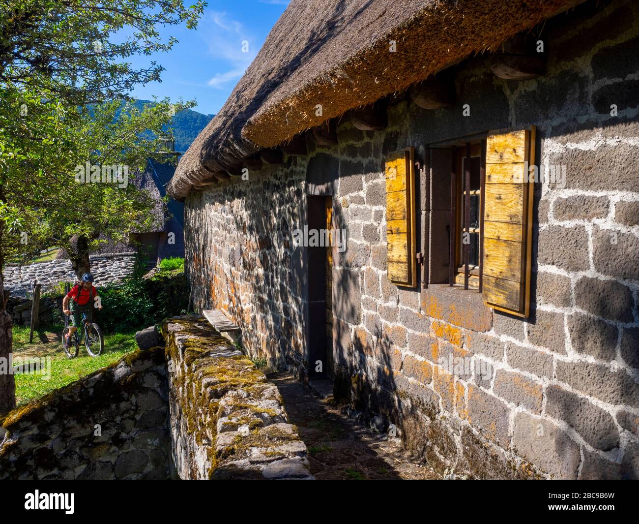 Mountain bikers on a single trail past an old mountain farm, Chaumière de Granier in Nierveze, Thiézac. Monts du Cantal, Massif Central, Cantal France Stock Photo