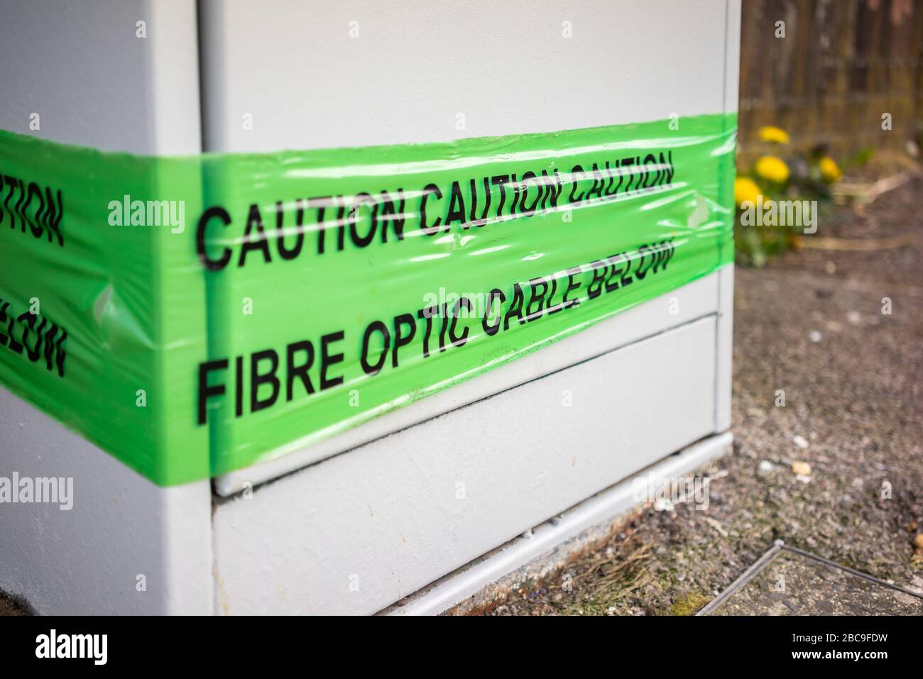 Broadband cable box with a warning on a banner stating 'Caution - Fibre optic cable below' along a pavement in Southampton, England, UK Stock Photo