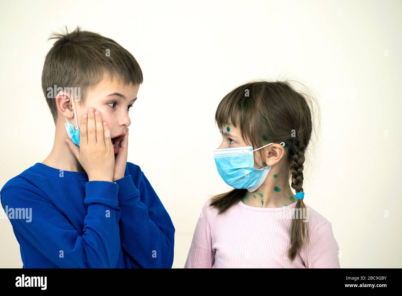 Boy and girl wearing blue protective medical mask ill with chickenpox, measles or rubella virus with rashes on body. Children protection during epidem Stock Photo