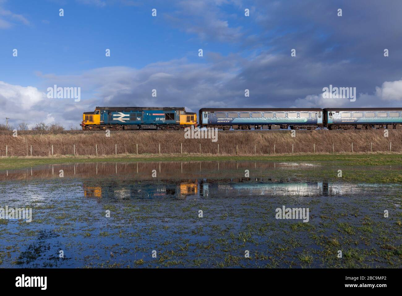 Direct Rail Services class 37 locomotive 37401 reflected in a flooded field while working a Northern Rail passenger service Stock Photo