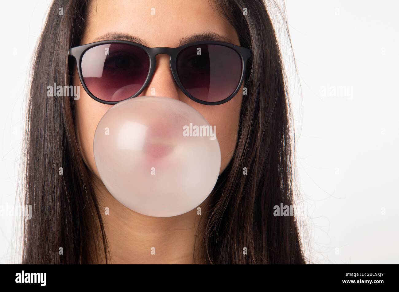 Brunette teenager girl with sunglasses blowing a bubble gum balloon Stock Photo