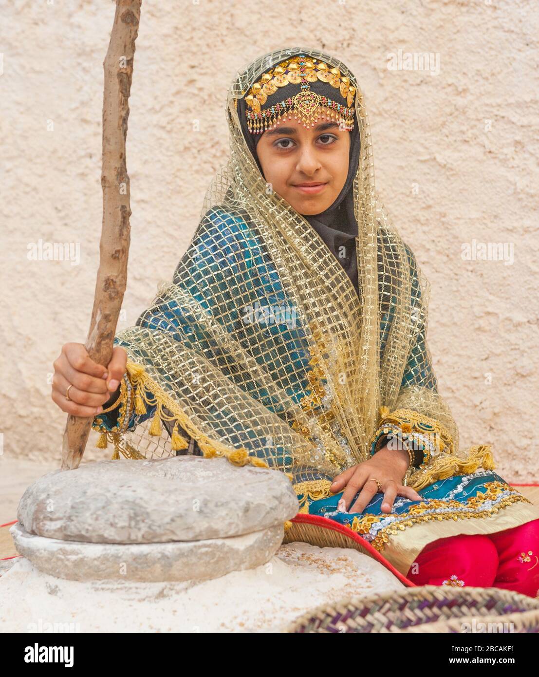 Portrait of an unidentified young woman in traditional Omani tribal dress, relaxing next to a grinding stone. Stock Photo