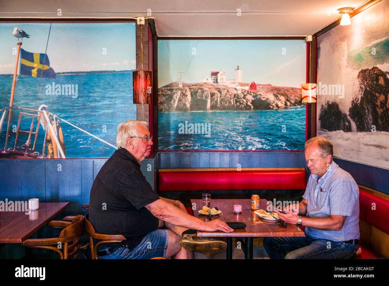 Sweden, Bohuslan, Orust Island, Ellos, two men in small cafe with poster of Nubble Light from York Beach Maine, USA Stock Photo