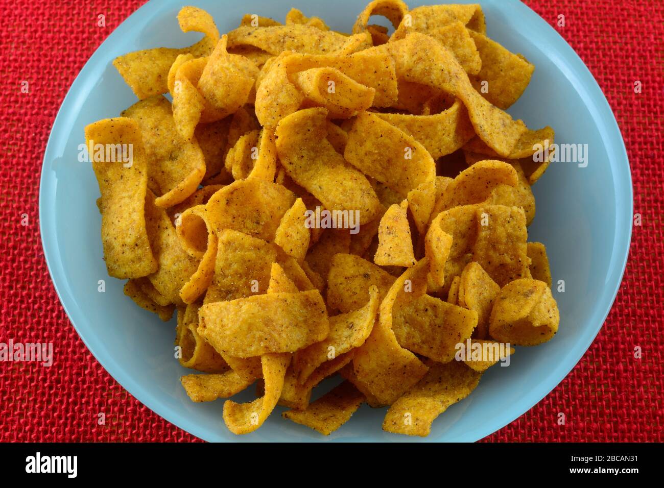 Spicy chili and cheese flavored corn chip strips in blue bowl on red