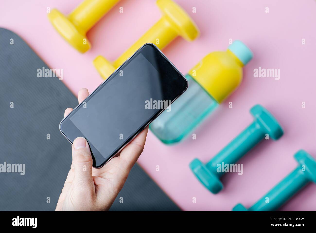 Hand taking a picture of dumbbells and bottle of water lying on a mat. Top view. Stock Photo