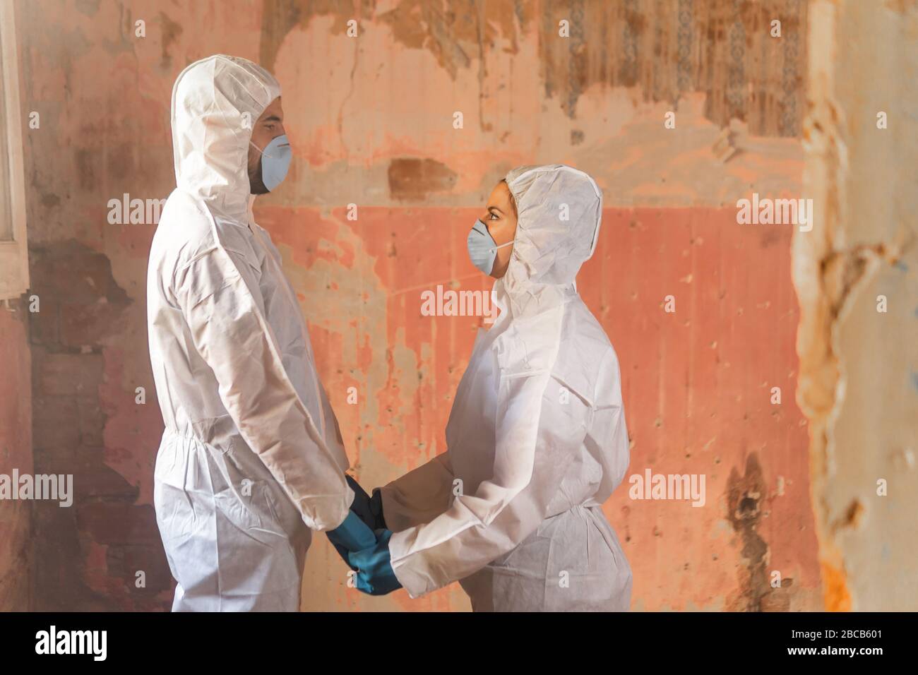 Couple of virologist doctors and scientists wearing biohazard protective suits and holding hands full of hope after a nuclear core meltdown disaster Stock Photo