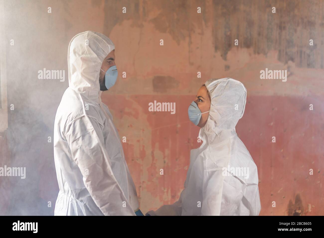 Couple of virologist doctors and scientists wearing biohazard protective suits and holding hands full of hope after a nuclear core meltdown disaster Stock Photo