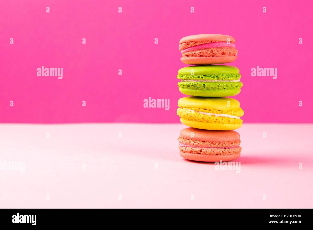 Multi-colored macaroons stand in a pile on a pink table Stock Photo
