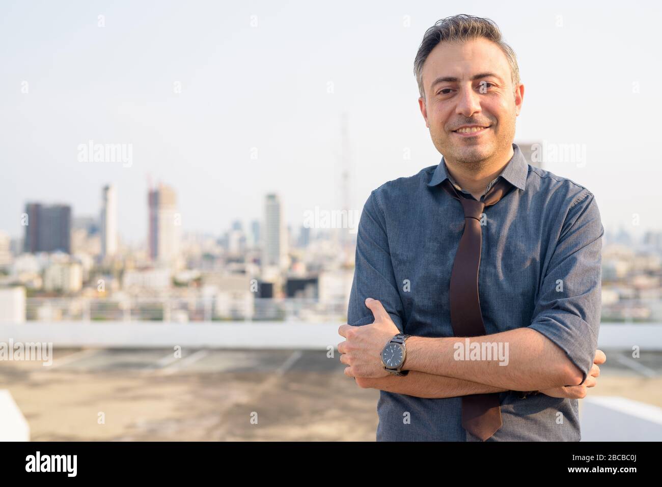 Happy mature handsome businessman smiling with arms crossed in the city ...