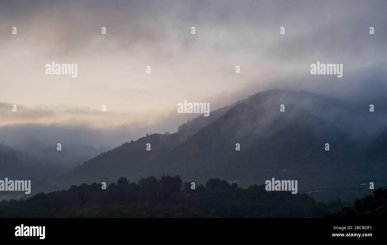 A view of a dark distant hill covered by mist and low cloud just before dawn with first light in the sky Stock Photo