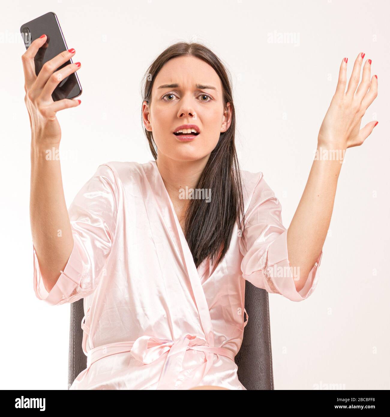 Attractive young brunette woman wearing a pink nightgown, in frustrated pose with phone in her hand. Royalty free stock photo. Stock Photo