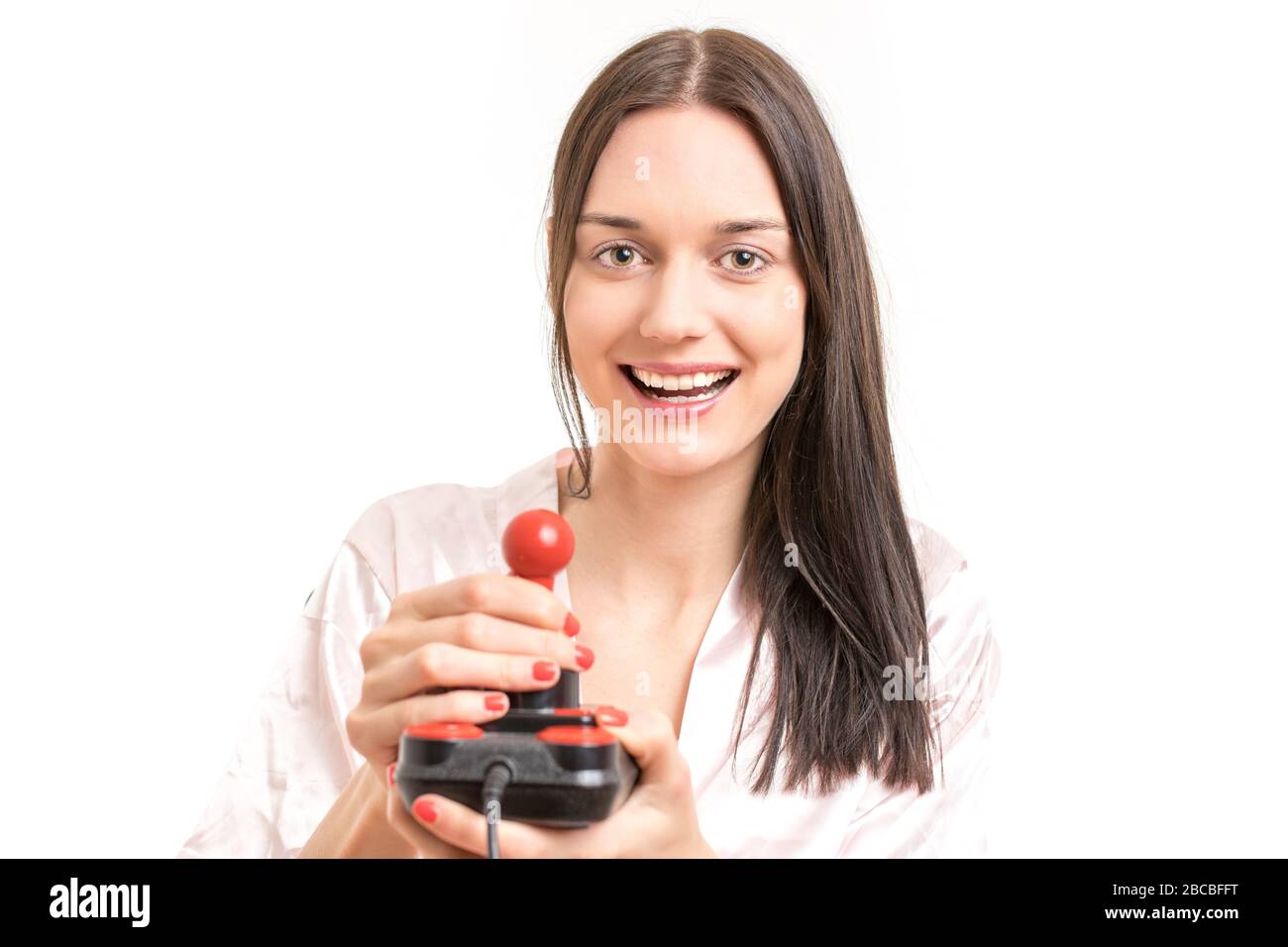 Attractive young brunette woman wearing a pink nightgown, laughing while operating a joystick. Royalty free stock photo. Stock Photo