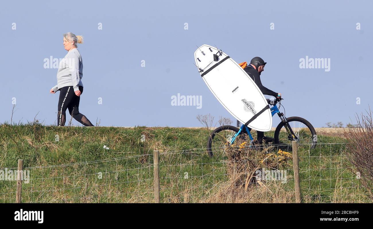 A surfer cycles with a surfboard on his back on Tynemouth Longsands Beach. Issue date: Saturday April 4, 2020. Banished from the waves by the coronavirus crisis, Britain’s surfing community is being forced to find increasingly creative ways to keep its lust for the sport alive. From Tynemouth to Newquay, shut-up surf shops scatter the deserted promenades and only the bravest and hardiest of individuals are stretching lockdown laws to their limits in order to head into the ocean. See PA story sport Coronavirus Surfing. Photo credit should read: Owen Humphreys/PA Wire. Stock Photo