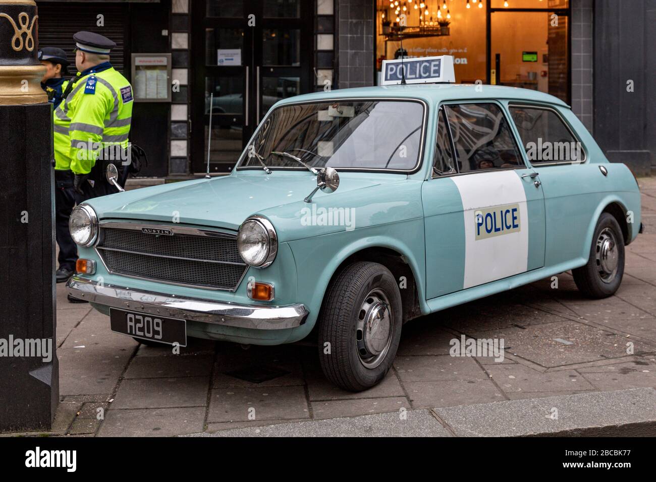 A policeman stands next to a vintage 1973 Austin 1100 MKII police car, London, England Stock Photo