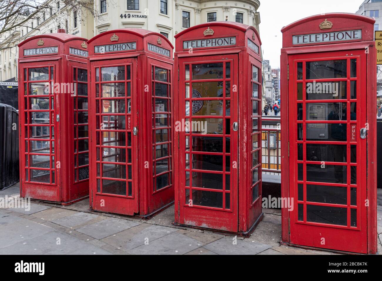 Four red traditional and heritage telephone boxes stand in a row on the Strand, London, England, UK opposite Charing Cross Station. Stock Photo