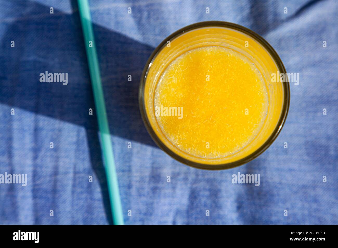 A glass of fresh citrus juice on a blue background. Top view, drink in the sunlight. Stock Photo