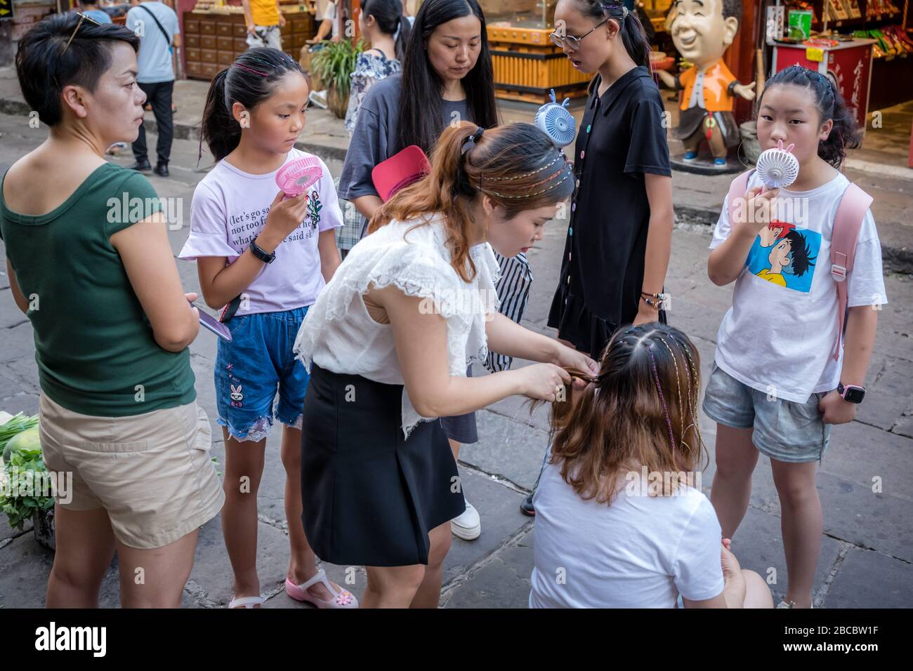 Chongqing, China -  August 2019 : Woman braiding friends hair on the stret in Ci Qi Kou Old town Stock Photo
