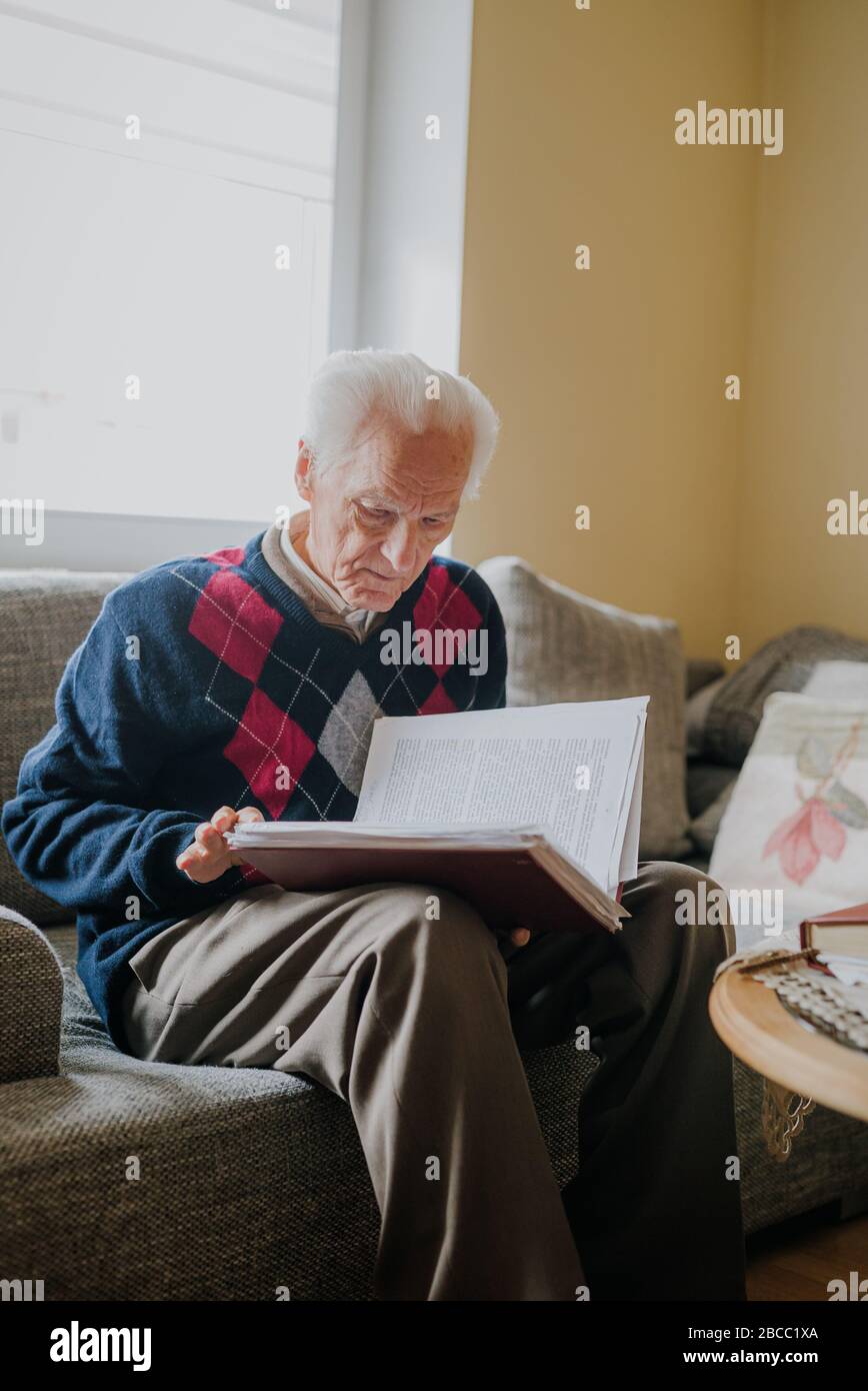 Old man reading book sitting on couch Stock Photo - Alamy