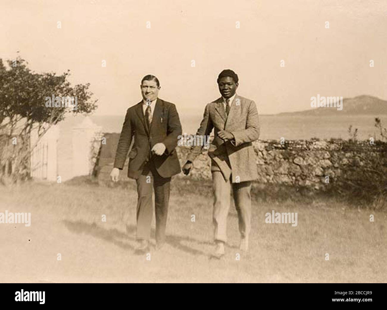 'This is Battling Siki from Senegal, World Light Heavyweight Boxing Champion, with his sparring partner, Frenchman Eugene Stuber. Siki was in Dublin to fight Bold Mike McTigue (aka Methuselah) who hailed from Kilnamona, Co. Clare. The two men are pictured outside the Claremont Hotel, Howth, Co. Dublin. The fight was on Saturday, 17 March 1923 (St. Patrick's Day) at La Scala Theatre, Dublin. McTigue won on points. Irish Times reporting on Monday 19 March was a little sniffy about the quality of the boxing: There was an almost total absence of those thrills and exciting incidents one is wont to Stock Photo