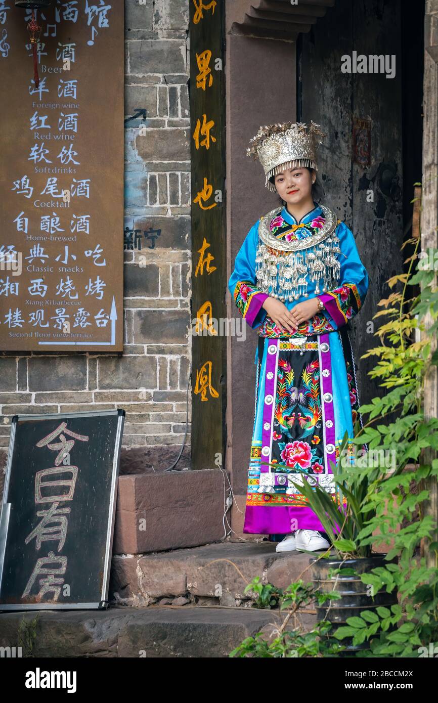 Feng Huang, China -  August 2019 : Beautiful Chinese woman dressed in traditional folk costume and posing for a picture outside the entrance to the ol Stock Photo