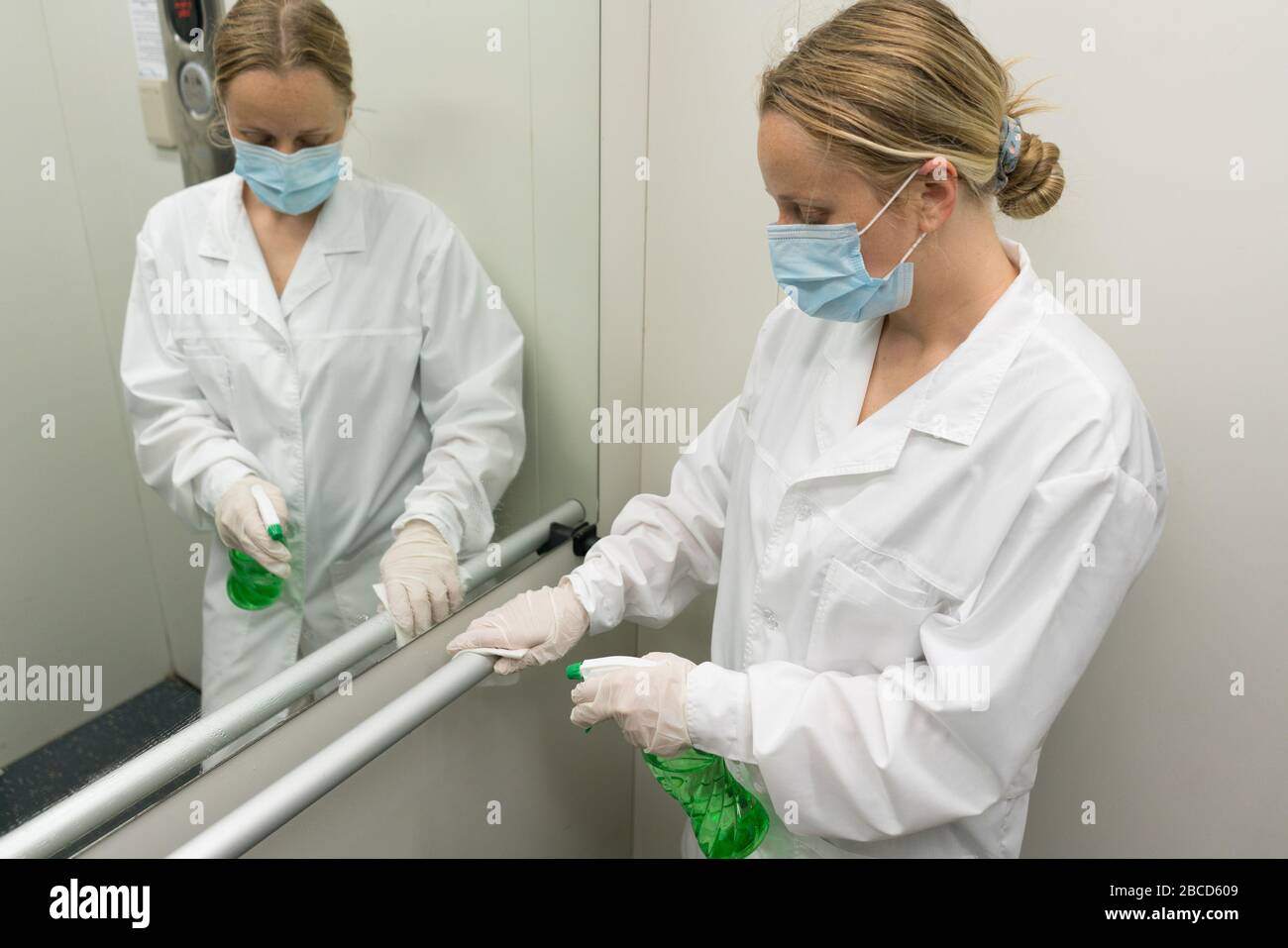 Woman using wet wipe and alcohol sanitizer spray to clean railing in ...