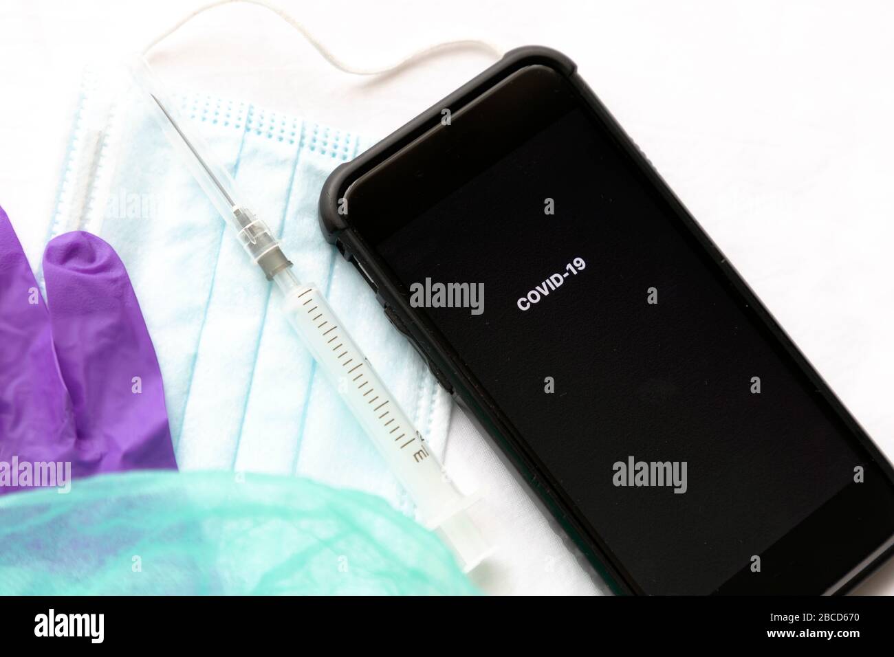 Gloves, mask, syringe with needle and phone on a white background. Phone with message COVID-19 and modern tracking applications. Stock Photo