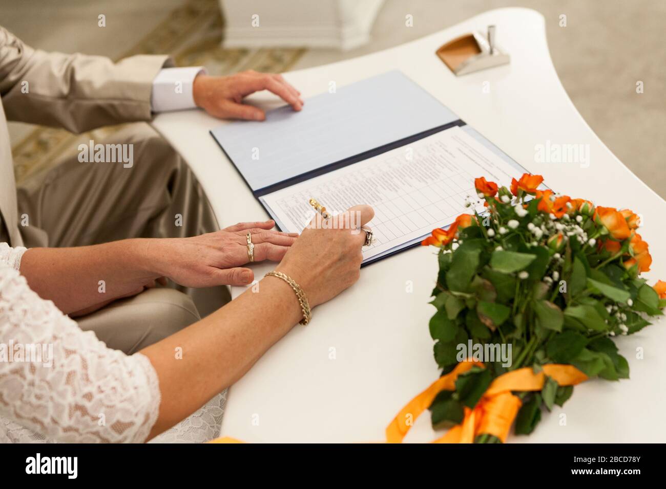 Bride signing wedding certificate while sitting at table on wed ceremony, hands close up view