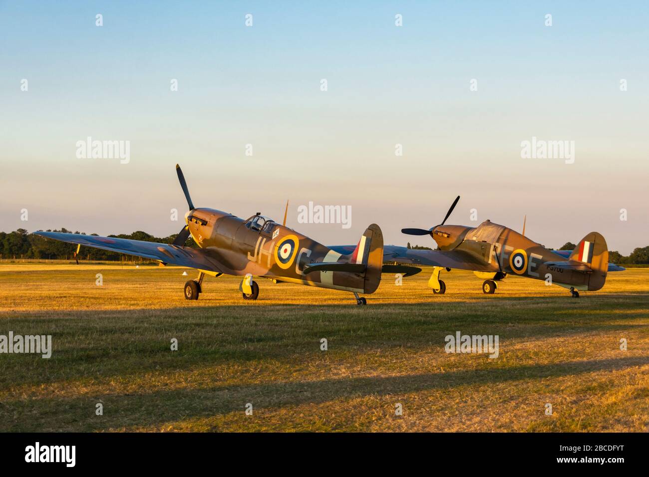 World War 2 Spitfire and Hurricane airplanes sit side by side in evening light at Headcorn Airfield Stock Photo