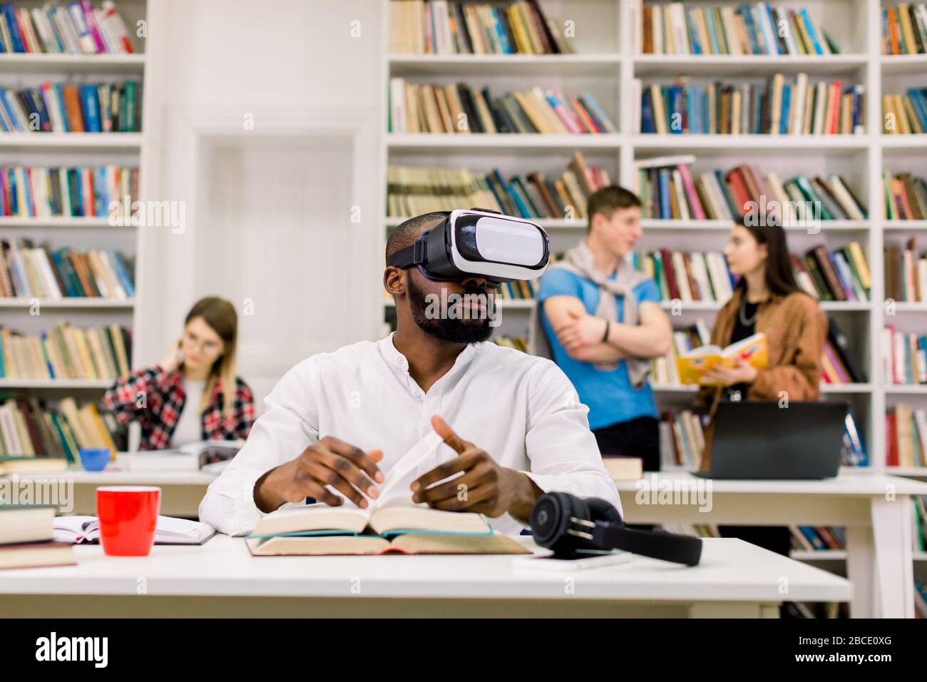 Black guy wearing vr goggles headset, reading book and using information  from virtual reality, sitting in modern library. Group of students studying  Stock Photo - Alamy