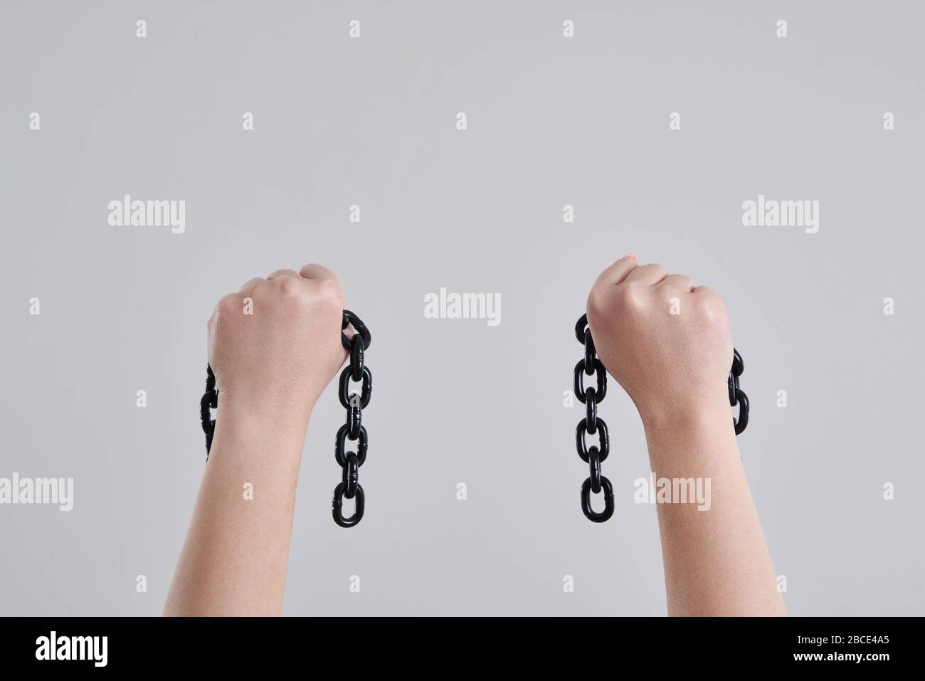 Female hands holding a broken metal chain over grey background with copy space Stock Photo