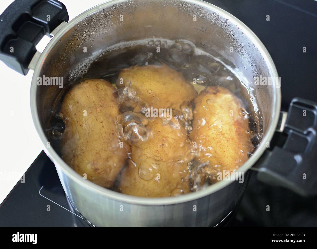 Top view of boiling whole potatoes in hot water in silver saucepan. Stock Photo