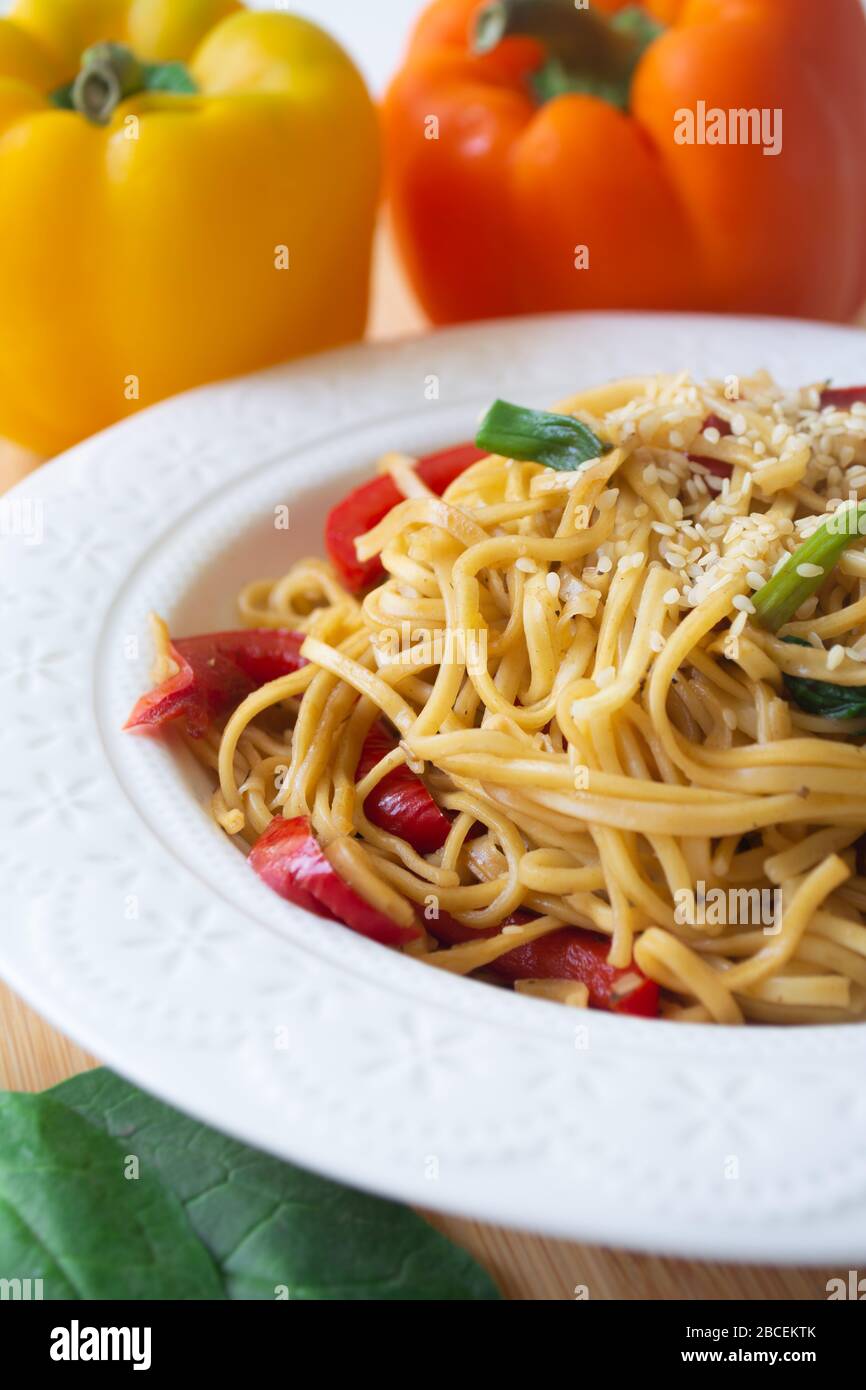 Chinese egg noodles in soy sauce with colourful bell peppers, greens and spring onions with sesame seeds sprinkled on top Stock Photo