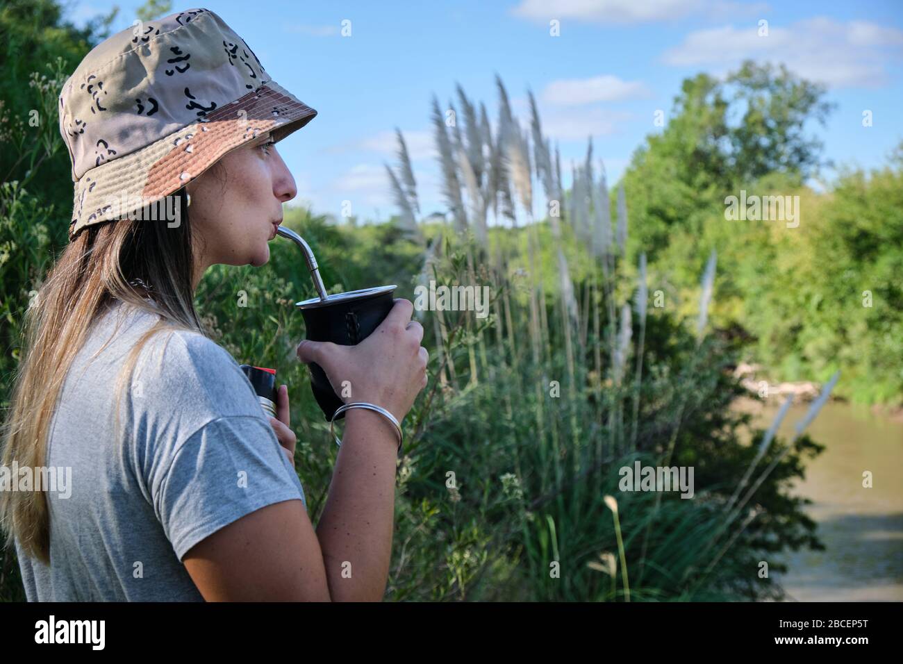 a beautiful girl model drinking yerba mate hot infusion beside the river in Bel Ville City, Cordoba, Argentina Stock Photo