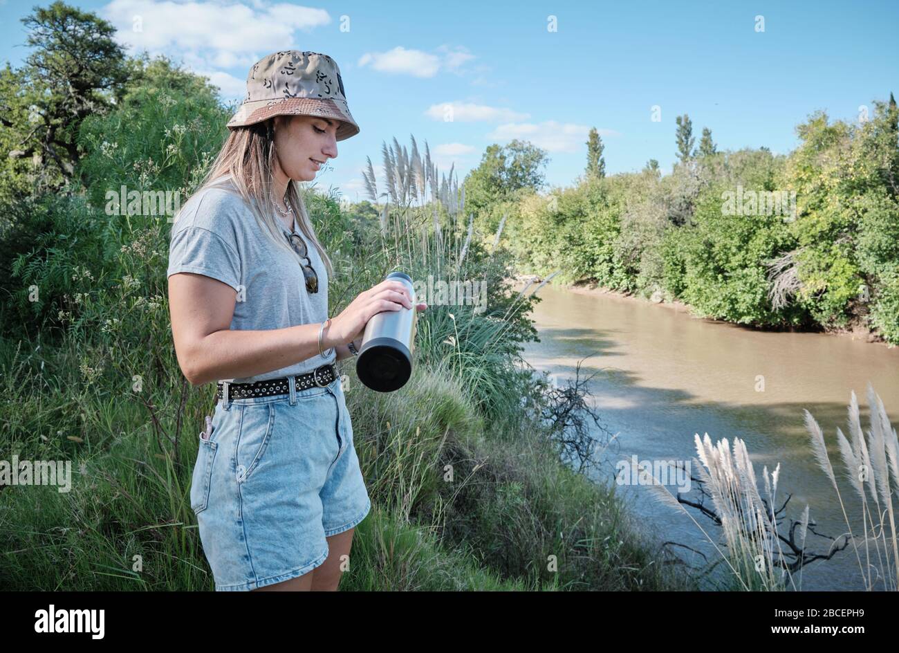 a beautiful girl model drinking yerba mate hot infusion beside the river in Bel Ville City, Cordoba, Argentina Stock Photo
