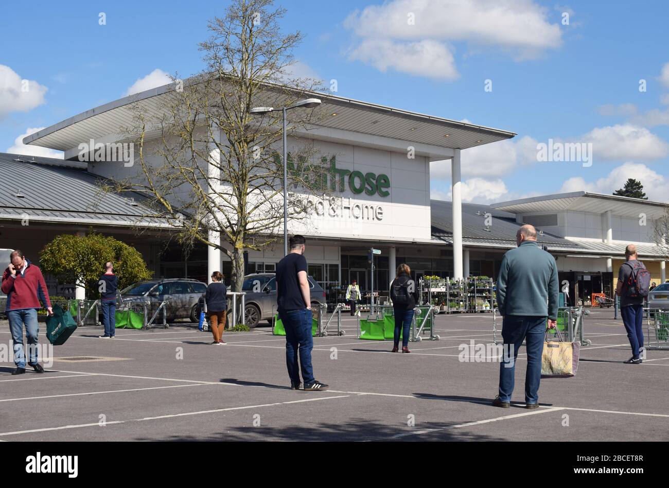 People queuing 2 meters apart in a car park while waiting to enter a supermarket to buy groceries in the UK during the Coronavirus Covid19 pandemic Stock Photo